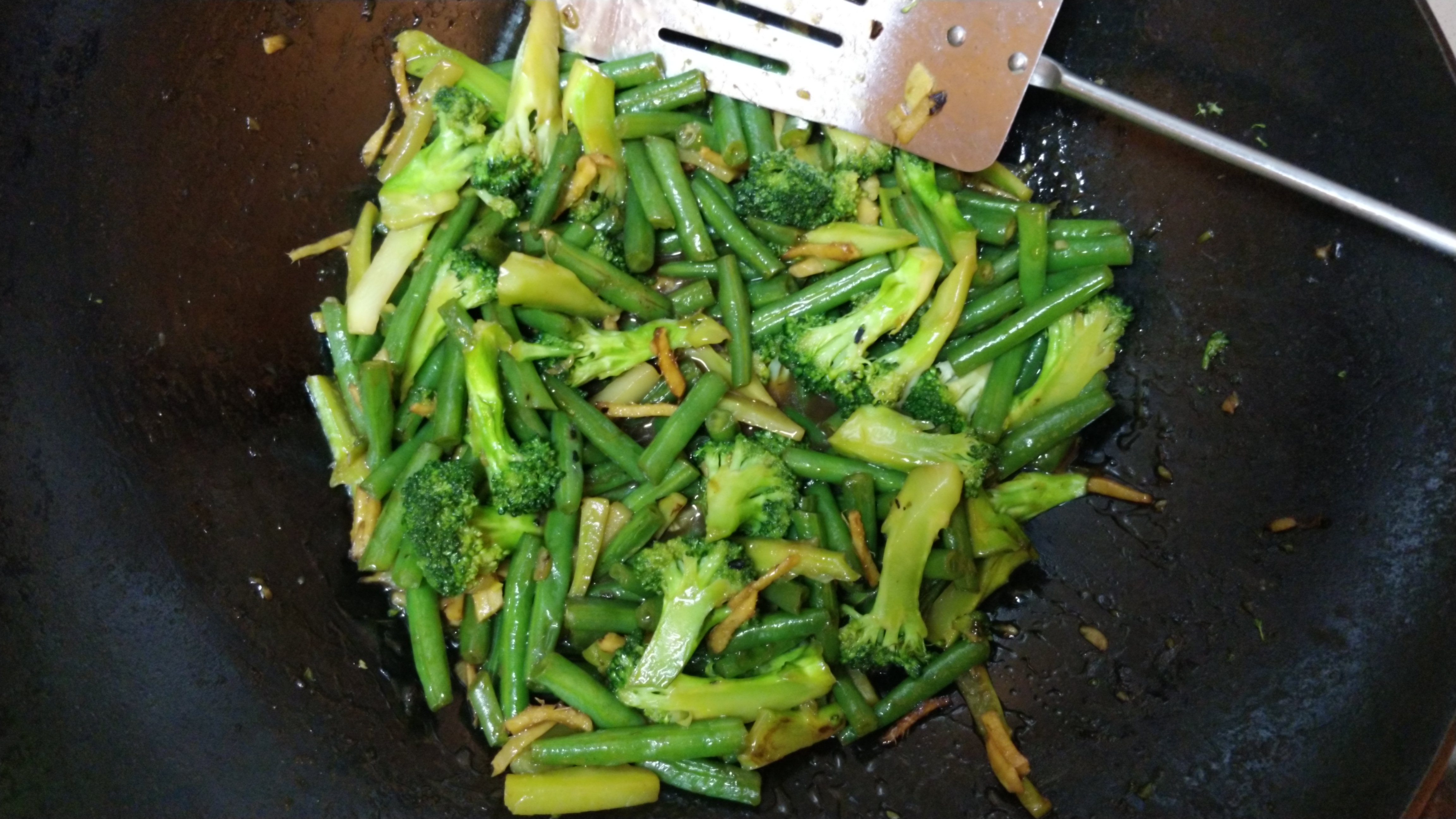 stir fried broccoli and green beans with ginger and garlic, in oyster sauce and shaoxing wine, in a wok on the stove
