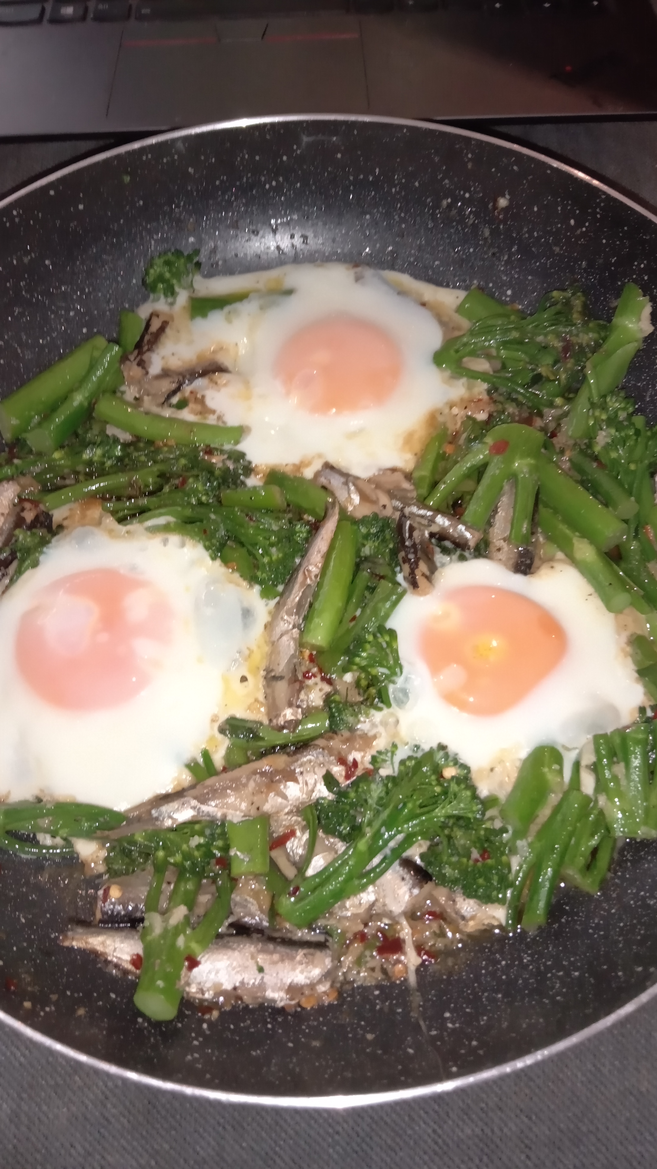 saucepan filled with fried Sardines, broccolini with garlic and chilli, and three perfect fried eggs