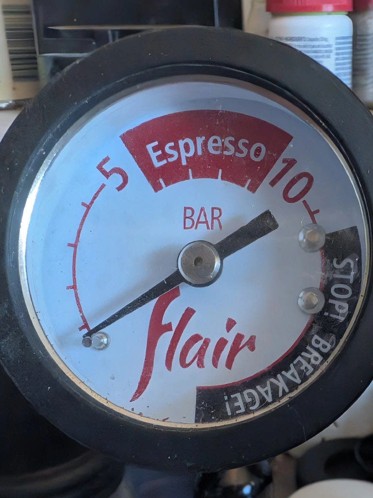 Flair 58 lever coffee machine&#39;s pressure gauge marked as showing pressure in bar with tick marks for each bar and numbers at 5 and 10 bar. A red area between 5 and 10 is labeled &#39;Espresso&quot;. A black area from 12 bar onwards is labeled  &#39;STOP! BREAKAGE!&quot;
