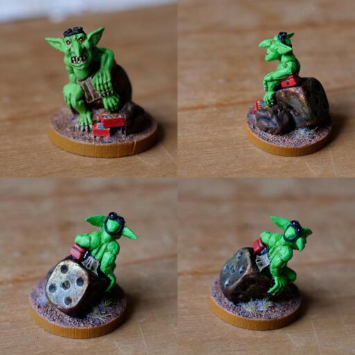 Four shots of the same wargaming miniature (different angles). The sculpt is of a goblin, sat on a dice (painted to look rusty), with a bag at his feet spilling out boxes (painted to look like the boxes Warhammer miniatures came in the mid 1990s). The goblin is wearing a loin cloth and leaning on a small, red money box (the lockable kind often used by traders running stalls at conventions).  The goblin is about an inch tall and there's small tufts of dried grass on the base of the model.