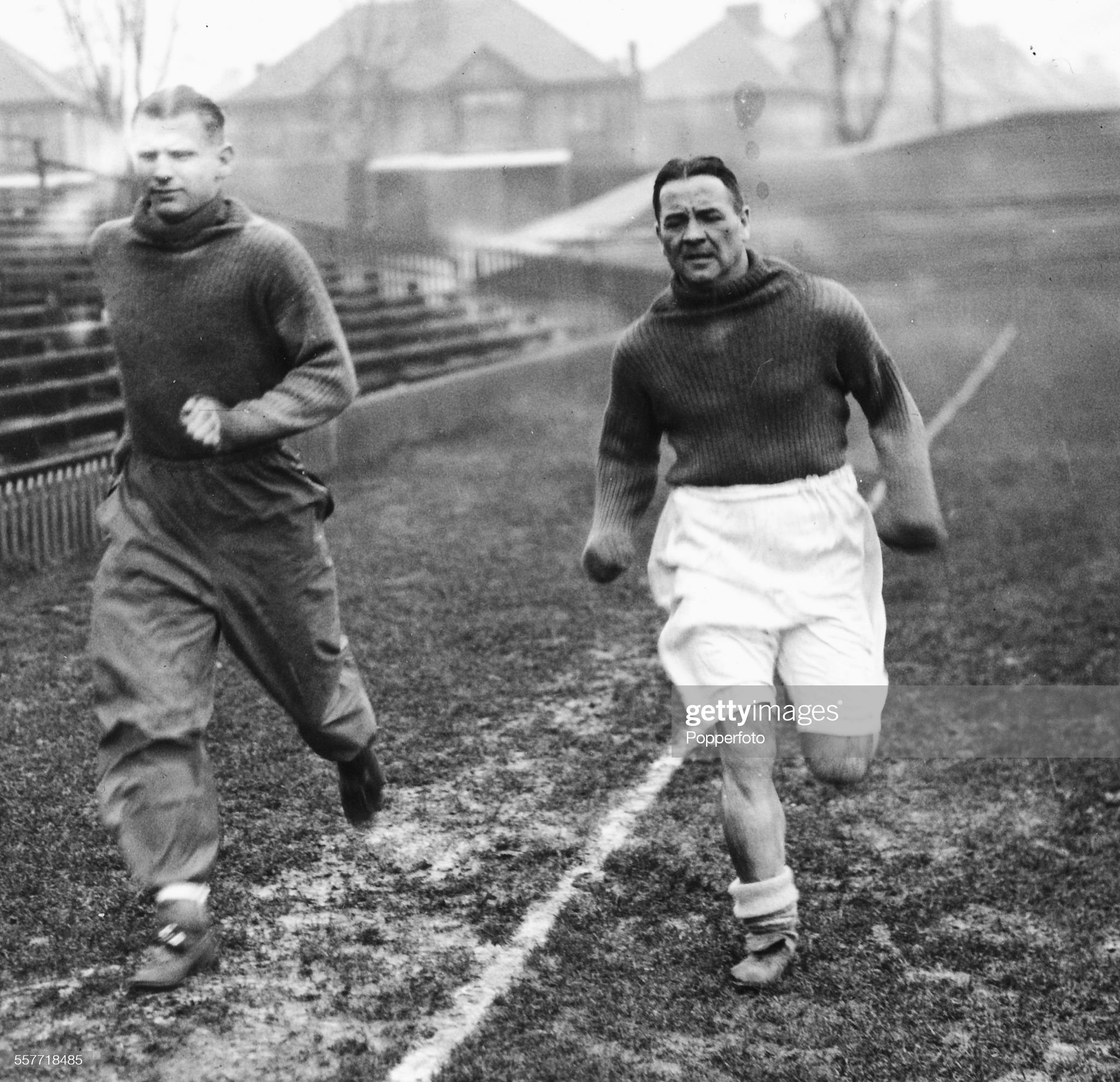 Arsenal football players Alex James (1901-1953) (right) and Cliff Bastin (1912-1991) (wearing waterproof trousers) running through the mud during training for the upcoming cup-tie in Brighton, England, circa 1935. (Photo by Popperfoto via Getty Images/Getty Images)