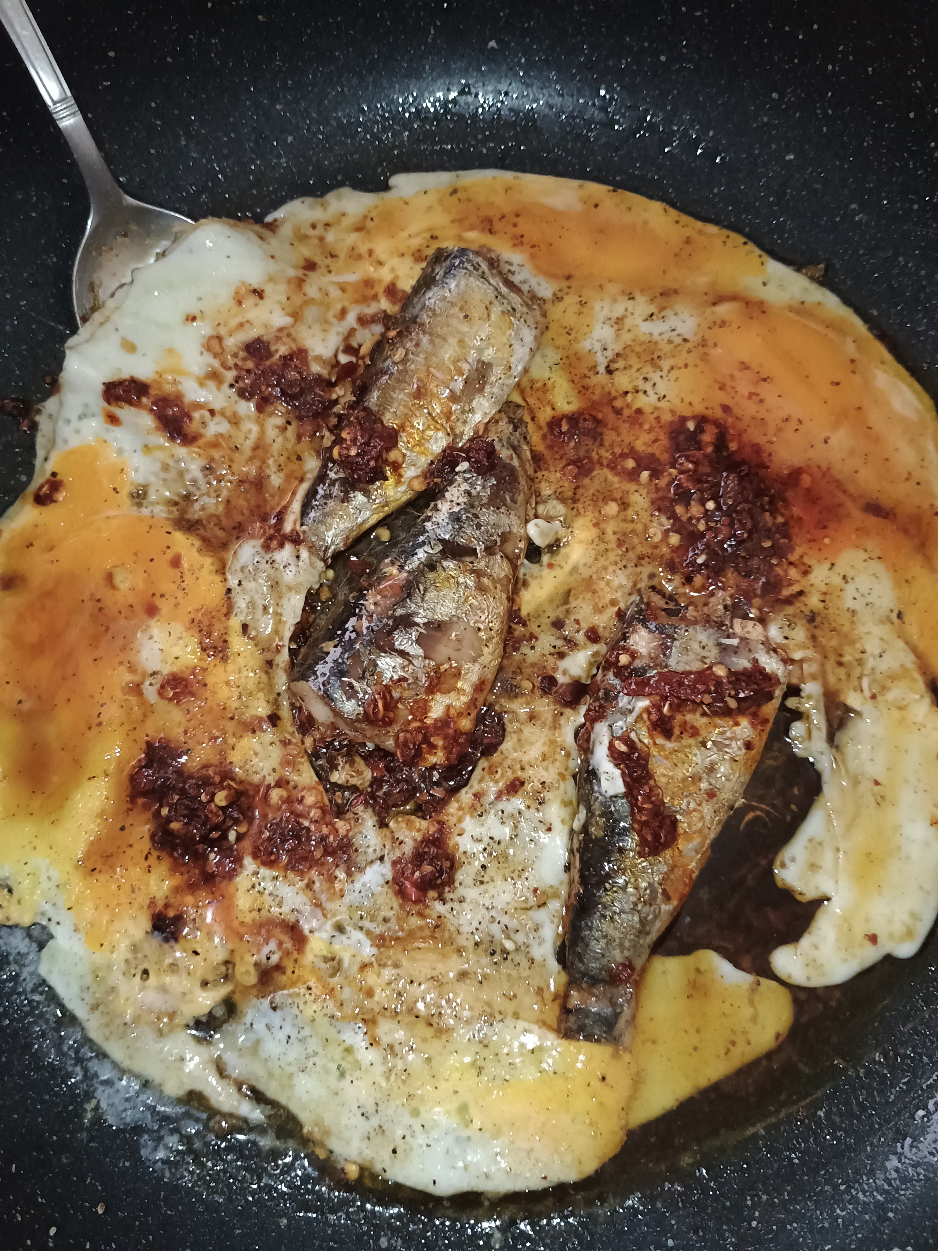 image of three sardines with two fried eggs, chilli crisp, and a splash of soy sauce in a frying pan!