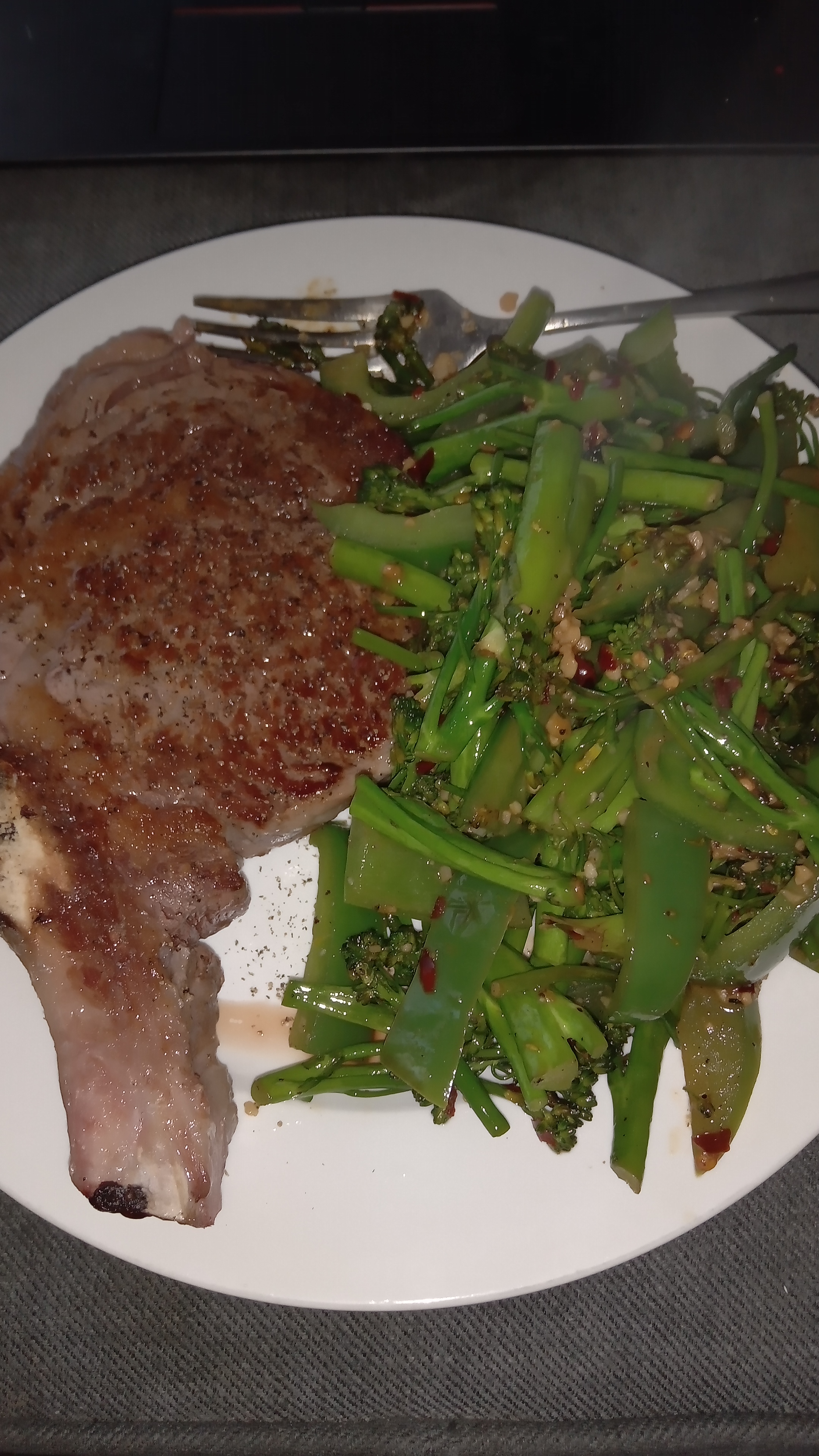 ribe eye steak on a plate with sauteed broccolini and capsicum