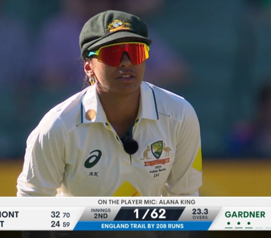 Photo of Alana King in cricket whites during a game. The lower third says "On the Player Mic: Alana King".