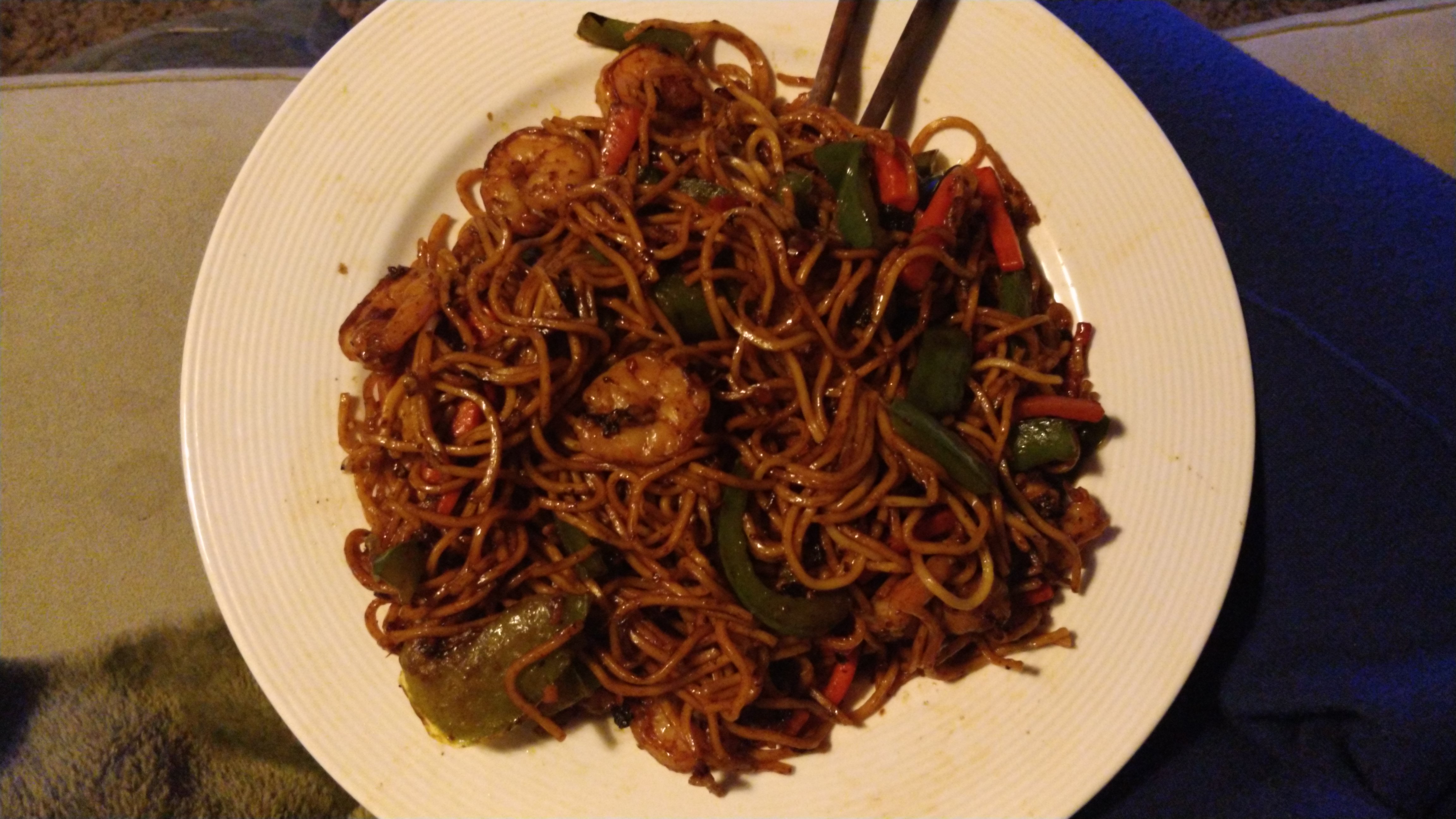 plate of yellow wheat noodles with prawns, carrot and green capsicum in a glistening dark sauce mixed through